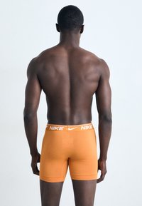Oranžové Nike boxerky s bielou elastickou gumou, pohľad zozadu. Tkanina vyzerá hladko s priliehavým strihom.