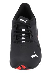 Svart sportskor med texturerad ovandel, vita accenter och röd sula. Har snörning, perforeringar och Puma-logotyp på sidan.