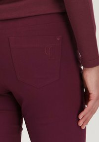 Bordeauxkleurige broek met een achterzak voorzien van een geborduurd logo en een gladde, rekbare textuur. Het ontwerp heeft een strakke pasvorm met een nette silhouet.