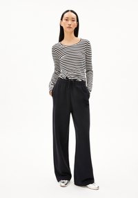 Gestreiftes Langarmoberteil in Schwarz und Weiß, kombiniert mit locker sitzenden Marineblauen Hosen, die einen elastischen Bund und seitliche Taschen haben. Silberne Schuhe.
