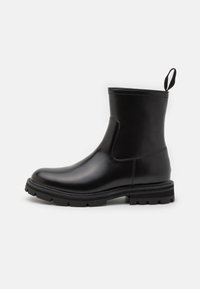 Botas de tobillo a prueba de agua en negro, con un acabado de cuero suave, paneles laterales elásticos y una suela de goma resistente para mayor tracción. Asa en la parte trasera.