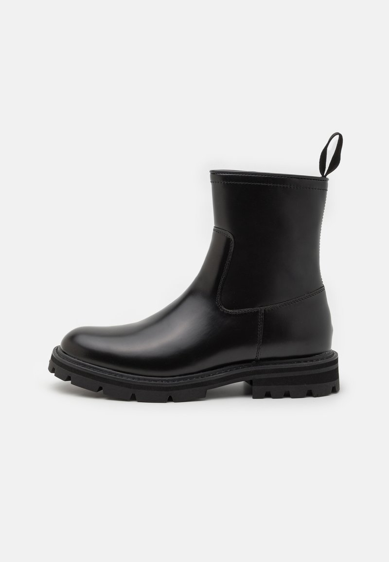Botas de tobillo a prueba de agua en negro, con un acabado de cuero suave, paneles laterales elásticos y una suela de goma resistente para mayor tracción. Asa en la parte trasera.