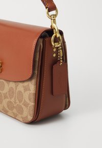 Sac à main en cuir brun avec un corps beige texturé présentant un motif circulaire. Accents en métal doré et une étiquette avec le logo "Coach" attachée.