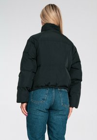 Czarna kurtka puchowa z wysokim kołnierzem, krótkim krojem i widocznymi szwami, w połączeniu z niebieskimi dżinsami z wysokim stanem.