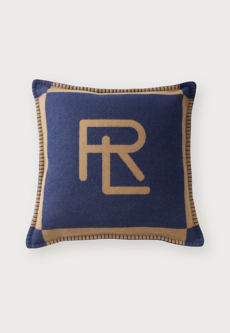 Cuscino blu navy con un bordo beige, con un logo dorato ben evidente. Texture del tessuto morbida con cuciture a contrasto lungo i bordi.
