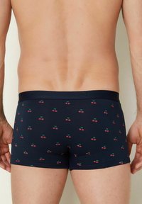 Boxer in blu navy realizzati in tessuto elasticizzato, caratterizzati da un motivo a ciliegie ripetuto in rosso e verde, con una vita morbida ed elastica.