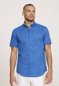 Chemise à manches courtes bleu, en tissu texturé, avec un col et six boutons sur le devant.