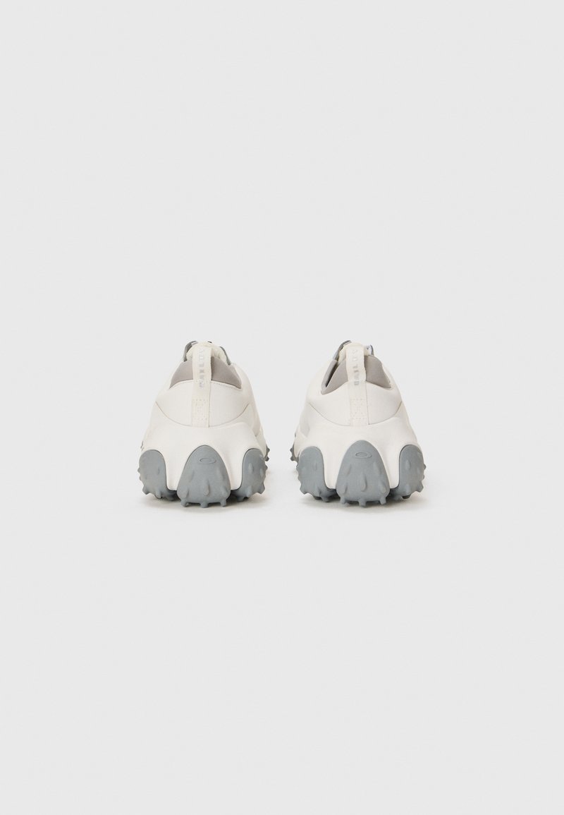 White slip-on shoes with a textured gray sole, featuring rounded edges and a heel tab for easy wear. Smooth upper material with minimal design.