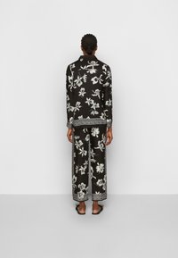 Zwart bloemen pyjama set met een lang- mouwshirt en wijde broek, versierd met witte bloemenpatronen en ingewikkelde randaccenten.