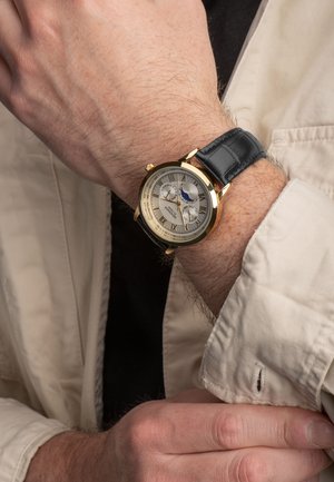 Montre-bracelet en ton or avec un cadran texturé argenté, un bracelet en cuir noir, un indicateur de phase lunaire et des index en chiffres romains.