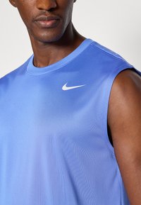 Blaues ärmelloses Sportshirt aus glattem Material. Verfügt über einen runden Halsausschnitt und ein kleines weißes Nike-Logo auf der linken Brust.