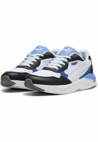 Pár bílých, černých a modrých tenisek Puma s bílými tkaničkami a silnými bílými podrážkami, nakloněných tak, aby ukázaly přední a boční detaily.