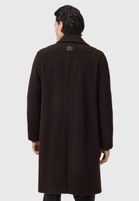 Brauner Wollmantel mit strukturiertem Finish, breitem Kragen und langen Ärmeln. Enthält einen Rückenschlitz und ein dezentes Markenetikett am Kragen.