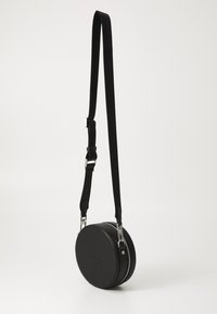 Black circular crossbody bag with a smooth faux leather exterior, silver zipper, and adjustable fabric strap.