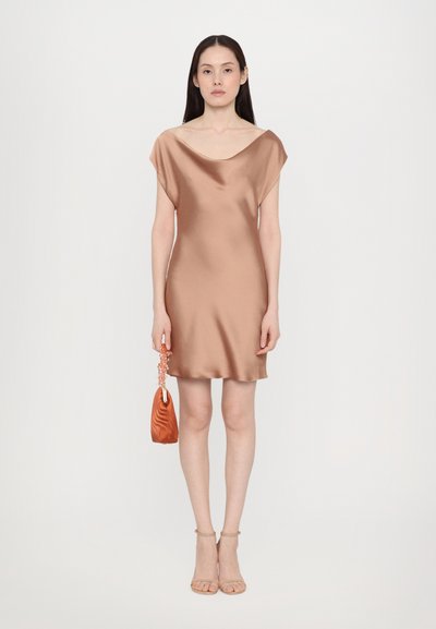 Satin mini kjole i en varm beige tone med en rundet udskæring og korte ærmer. Sammen med en struktureret orange håndtaske og gennemsigtige hæle.