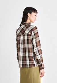 Bruin en crèmekleurig geruite blouse met lange mouwen, knoopmanchetten, ruches op de kraag en een geplooide achterkant. Lichtgewicht stof met een gladde textuur.