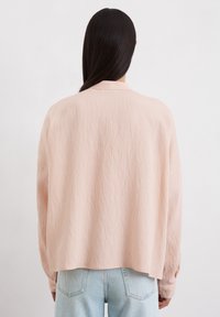 Blassrosa, gerippte, oversized Bluse mit Kragen, langen Ärmeln und fallenden Schultern, getragen über hellblauen Jeans.