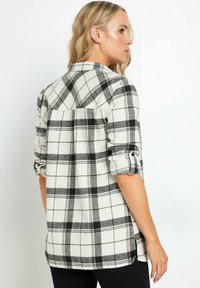 Creme- og sort ternet flannel skjorte med oprullede ærmer, knapmanchetter og en rygbælte. Blød tekstur og afslappet design.
