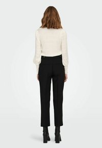 Suéter blanco de punto con mangas texturizadas, combinado con pantalones de tiro alto negros y botas negras de tacón cuadrado. Solo vista trasera.