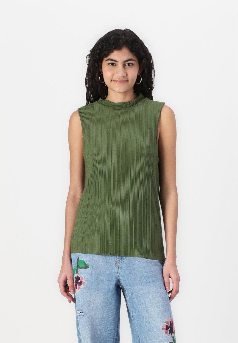 Ermeløs grønn topp med vertikale folder, høy krage og myk tekstur. Kombinert med lyseblå jeans med blomsterbroderi.