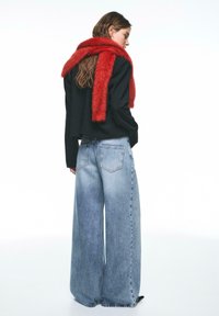 Maglione nero corto, jeans a gamba larga color azzurro chiaro e una sciarpa rossa soffice avvolta intorno al collo. L'outfit mostra una vestibilità comoda.