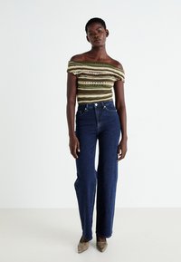 Striped off-shoulder top in green and cream, paired with high-waisted dark blue denim jeans and beige pointed-toe heels.