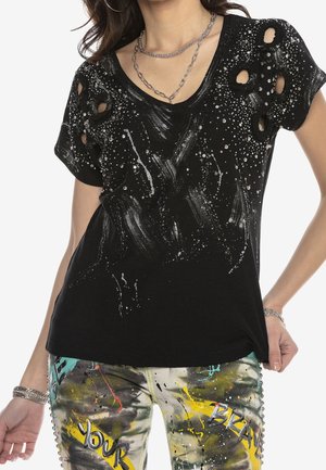 Black short-sleeve top with silver paint splatters and cutout holes, paired with colorful graffiti-style pants and silver chain necklaces.