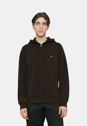 Felpa con cappuccio marrone con cerniera, cappuccio con coulisse, polsini a costine e un logo discreto sul petto; realizzata in tessuto morbido con una texture liscia.