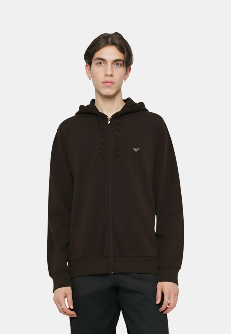 Felpa con cappuccio marrone con cerniera, cappuccio con coulisse, polsini a costine e un logo discreto sul petto; realizzata in tessuto morbido con una texture liscia.