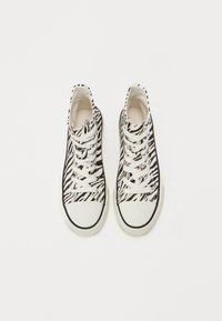 Svart og hvit høyhælte sneakers med et zebra-stripe mønster, med hvite snøring og gummisåle, glatt kanvas materiale.