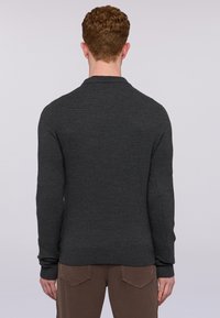 Maglione lavorato a maglia grigio scuro con maniche lunghe, polsini a costine e una superficie testurizzata, abbinato a pantaloni marroni. Vista da dietro.