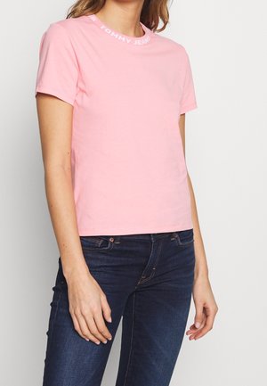 Różowy bawełniany t-shirt z okrągłym dekoltem, z nadrukiem nazwy marki "TOMMY JEANS" wzdłuż kołnierza. Krótkie rękawy, regularny krój.