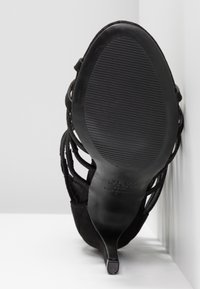 Sandale à talon haut noire avec semelle texturée et talon fin, photographiée par le dessous sur un fond blanc.