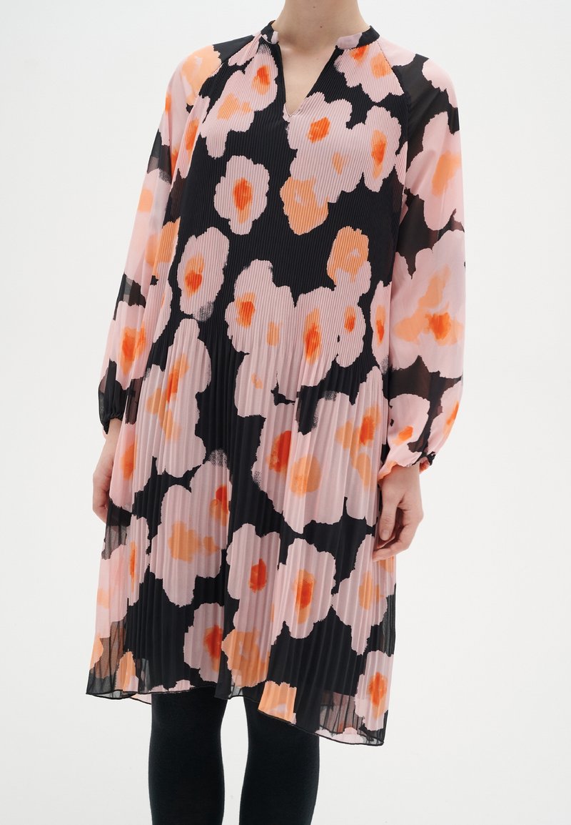 Plisserad klänning med långa ärmar i svart bakgrund och stora rosa och orange blommönster. V-ringning och samlade manschetter vid ärmarna.