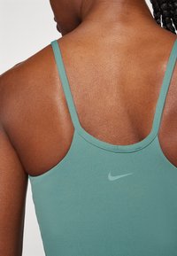 Primer plano de la parte superior de la espalda de una persona que lleva puesta una camiseta sin mangas Nike color teal con tirantes delgados y un pequeño logo de swoosh de Nike.