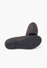 Zapato de tela marrón con forma curva y diseño minimalista. La suela exterior de goma negra flexible presenta patrones de corazones y flores.