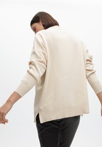 Felpa oversize beige con polsini e orlo a costine, dotata di fessure laterali per facilitare i movimenti, realizzata in un tessuto morbido e confortevole.