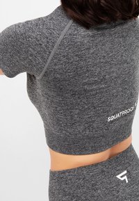 Crop top sportivo grigio con maniche corte, caratterizzato dal testo "SQUATPROOF", tessuto testurizzato e design aderente. I dettagli delle cuciture sono visibili.
