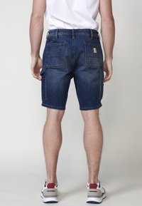 Tumši zili denim šorti ar kabatām, kuru dizainā ir divas aizmugurējās kabatas un sānu kabata ar rāvējslēdzēju, papildināti ar taisnu piegriezumu un apvilktu apakšmalu.