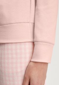 Lichtroze sweatstof, met ribgebreide manchetten en een zachte textuur; gecombineerd met roze geblokte broek.
