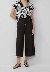 Svart och vit kortärmad blus med lövmönster, ihop med högmidjade, vida svarta byxor och platta svarta sandaler.