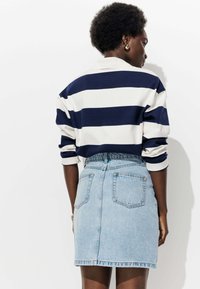 Pull à rayures à manches longues en marine et blanc, associé à une jupe en jean bleu clair avec des poches arrière et une silhouette ajustée.