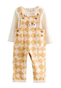 Salopette à carreaux jaunes et blancs avec deux poches avant, boutons en bois, et un haut crème à manches longues attaché avec un col à volants.