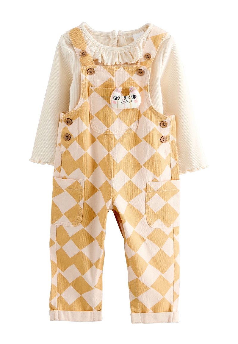 Salopette à carreaux jaunes et blancs avec deux poches avant, boutons en bois, et un haut crème à manches longues attaché avec un col à volants.