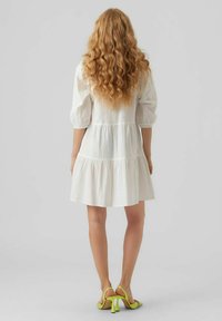 Robe blanche avec un design à volants, des manches bouffantes trois-quarts et une coupe décontractée. Associée à des sandales à talons hauts vert fluo.