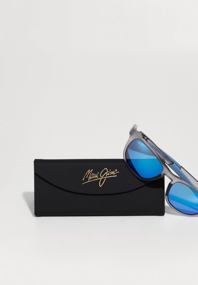 Okulary przeciwsłoneczne Maui Jim z szarym stelażem, niebieskimi lustrzanymi soczewkami i teksturowanym boku. Towarzyszą im czarne etui z złotym logo.