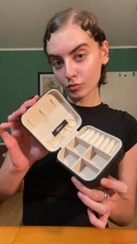 Black jewelry case with a cream interior, featuring multiple compartments and a labeled elastic band for organization. Zipper closure.