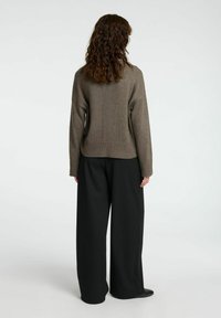 Maglione marrone a maglia con maniche lunghe, orlo a coste e vestibilità rilassata, abbinato a pantaloni neri a gamba larga e calzature nere lisce.