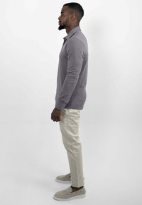 Lichtgrijs poloshirt met lange mouwen gecombineerd met crèmekleurige chino's, aangevuld met beige instapschoenen, weergegeven in een zijaanzicht.