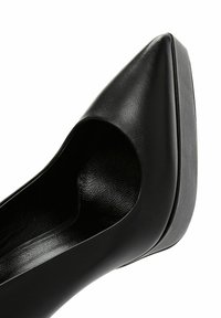 Zapato de tacón alto negro hecho de cuero suave, con punta afilada y un corte lateral abierto, que presenta una plantilla texturizada y un tacón sólido.